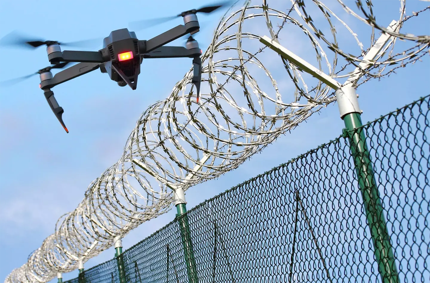 Image of a surveillance drone flying over a barbed wire fence
